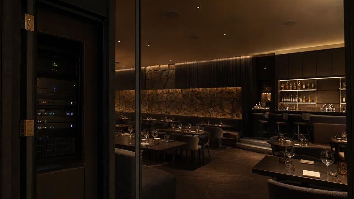 Restaurant audio installation in a refined New Jersey dining room with discreet ceiling speakers, a softly lit bar, and a labeled equipment rack