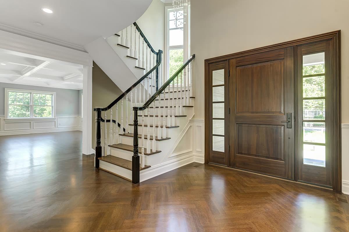 Sinclair Homes custom home builder foyer with a wood entry door, staircase, and finished hardwood floor