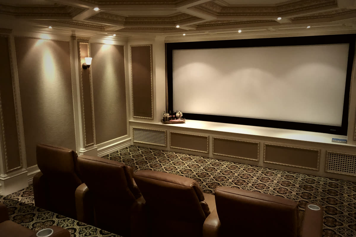 Restrepo Innovations traditional home theater with coffered ceiling, gold trim, fixed-frame screen, and brown leather seating