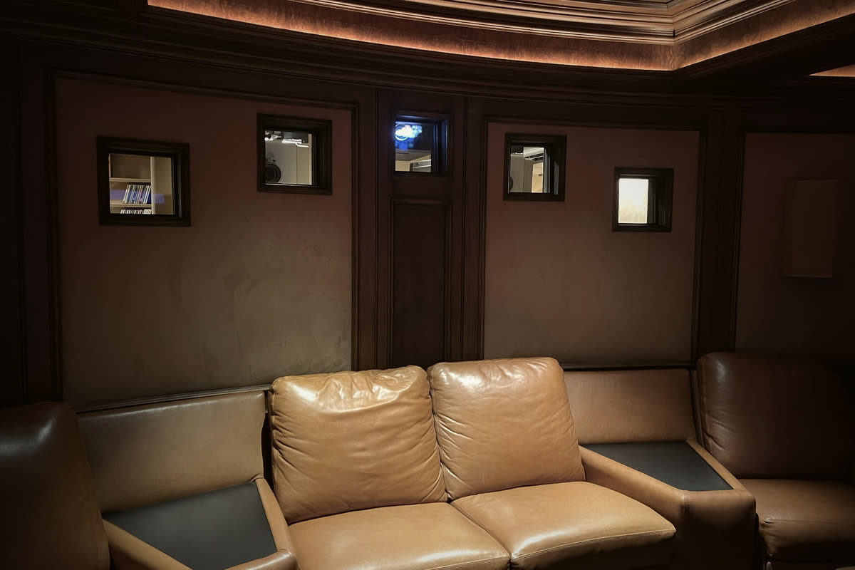 Restrepo Innovations home theater with brown leather seating and visible projection booth windows in a wood-trimmed ceiling soffit