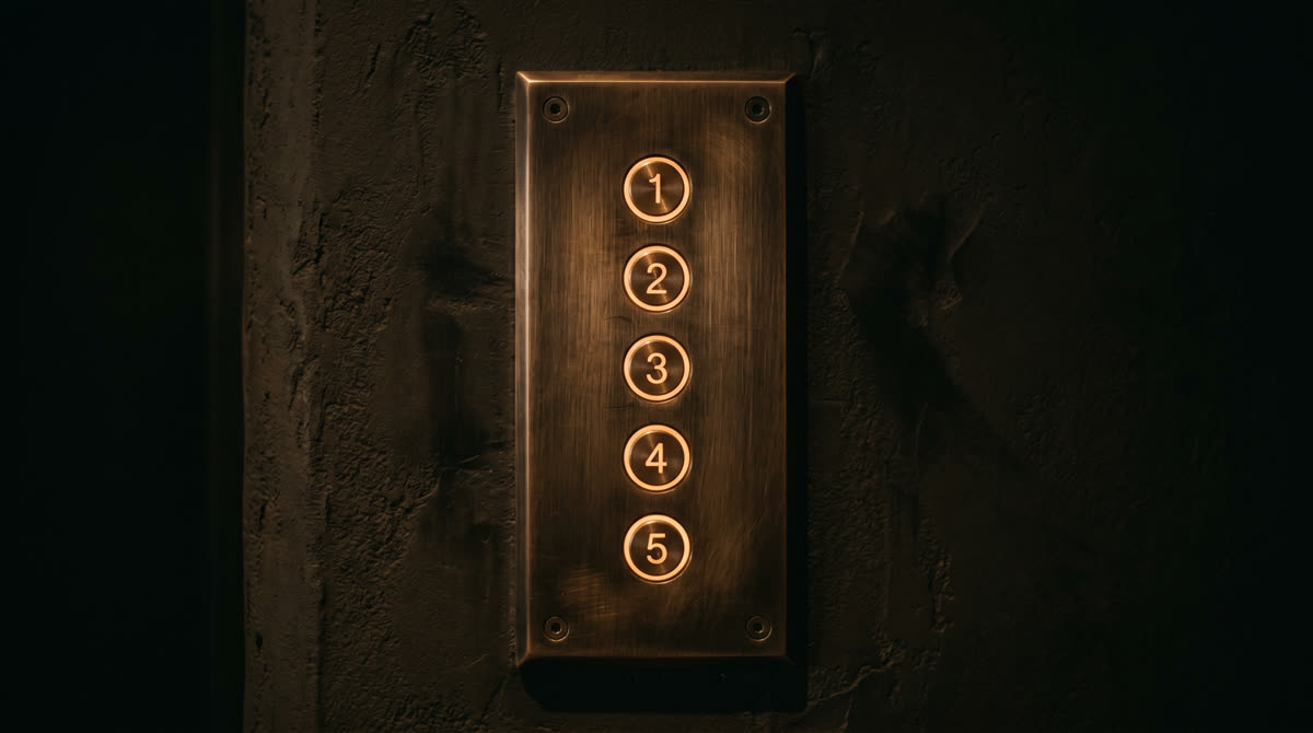 Architectural metal keypad faceplate in brushed bronze with amber-backlit circular buttons mounted on warm plaster wall